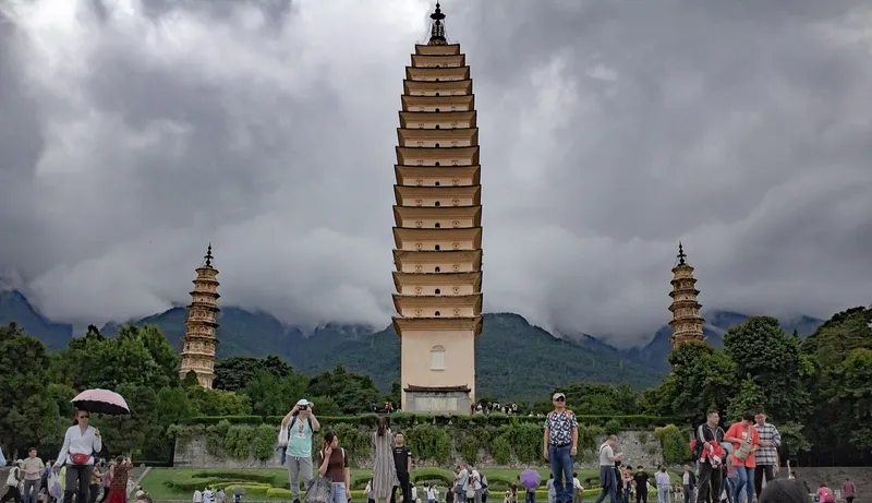 The Three Pagodas of Dali standing before the forested wall of the Cangshan mountains under clear sky