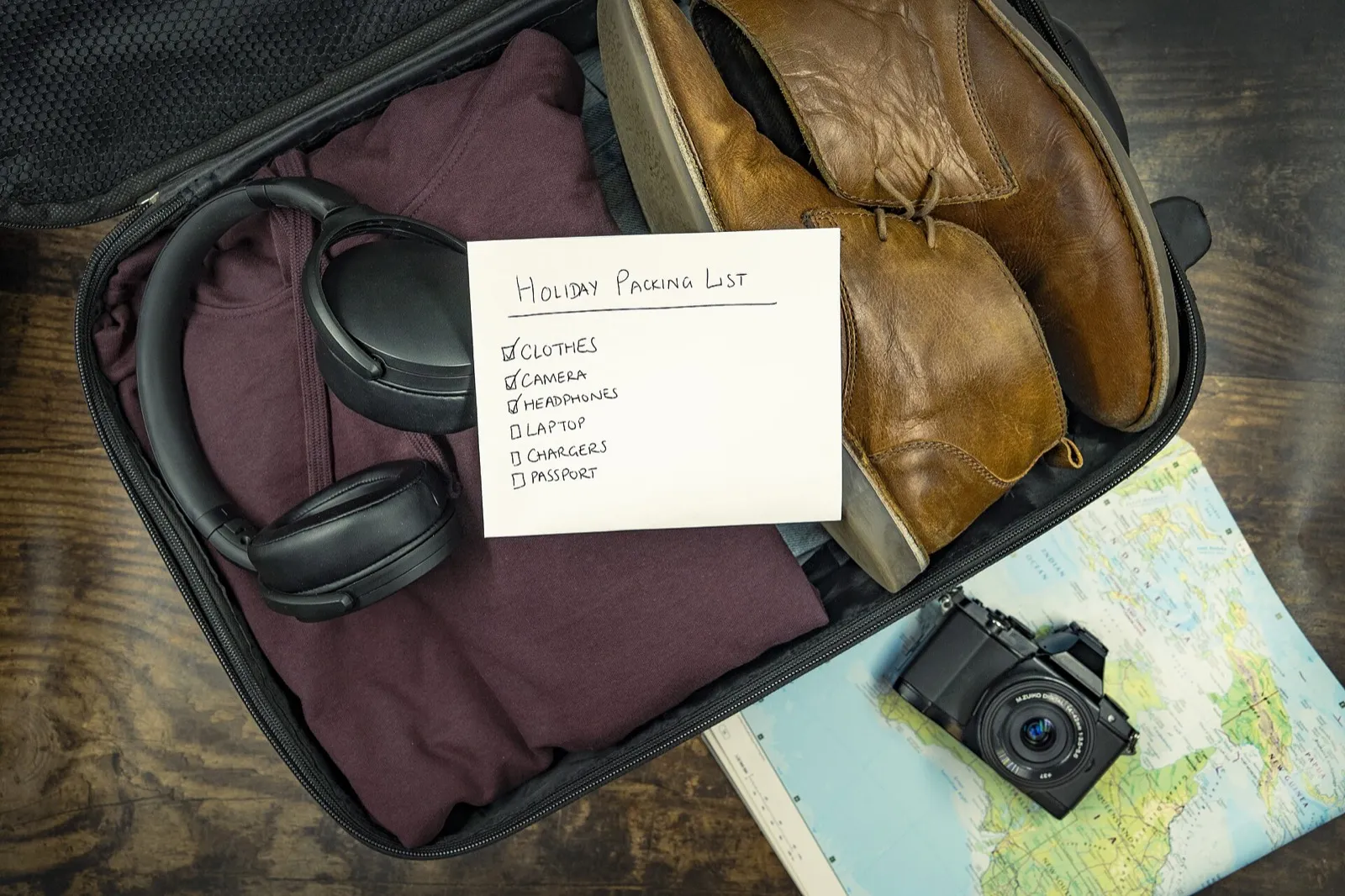A paper checklist beside a passport, phone, and charging cable on a desk before an international trip