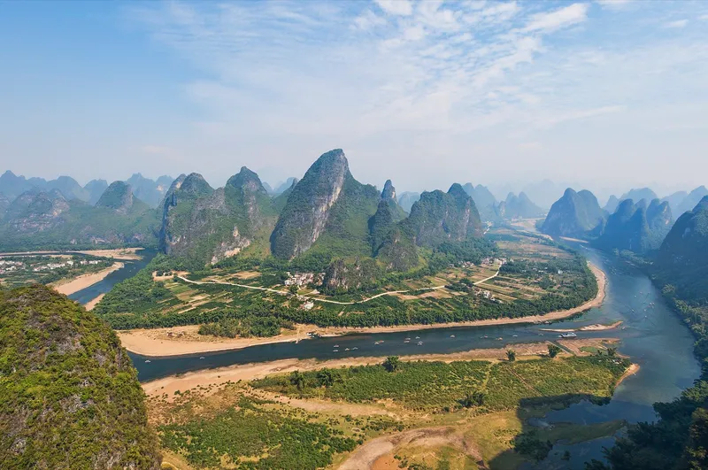 Limestone karst peaks rising from the Li River at first light, with a bamboo raft crossing the foreground